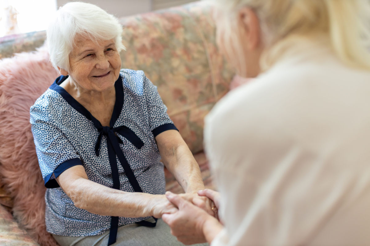 An in home senior care caregiver gently holds the hands of an elderly woman.